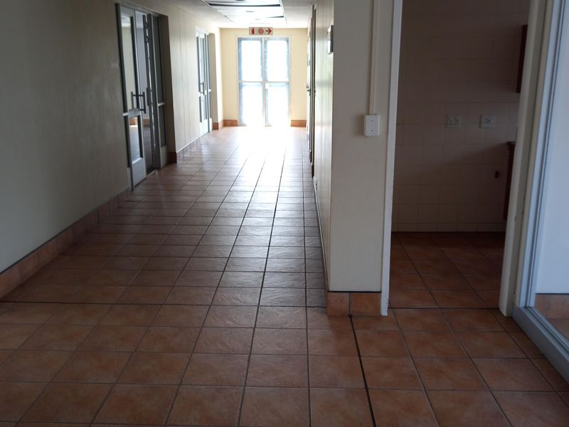 A long, tiled office hallway featuring a suspended ceiling with recessed lighting and access to multiple office spaces.