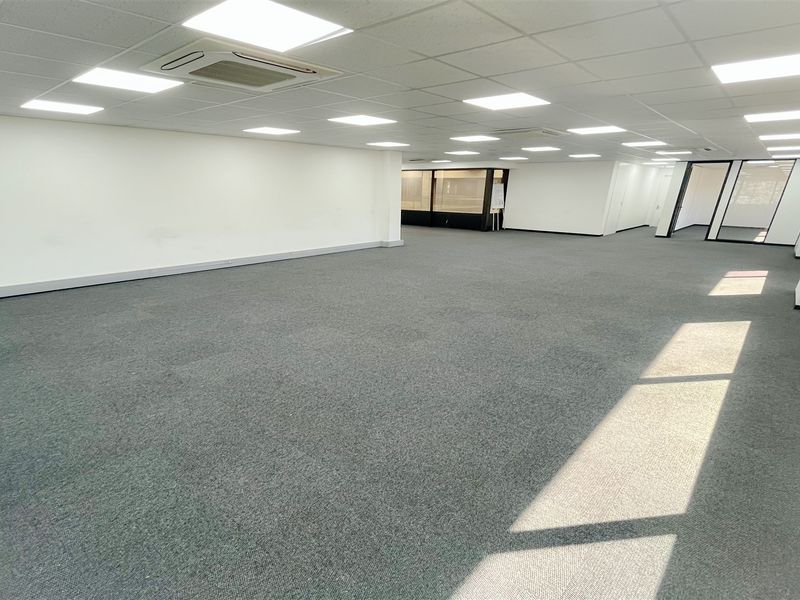 A spacious, open-plan office area featuring neutral carpeting, recessed LED lighting, integrated air conditioning, and modern glass partitions.