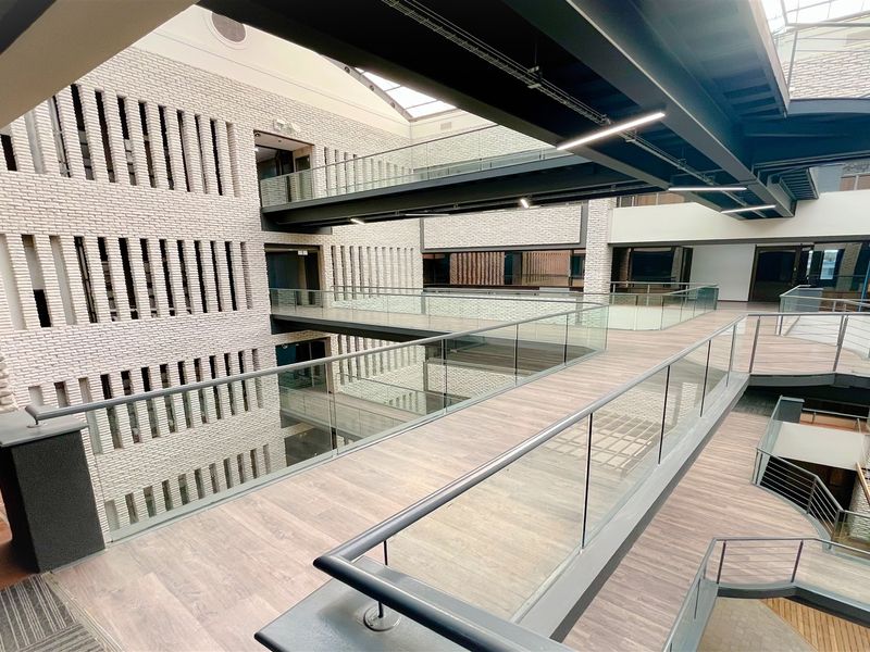 Modern office atrium featuring multi-level suspended walkways, glass balustrades, and architectural brickwork under a large skylight.