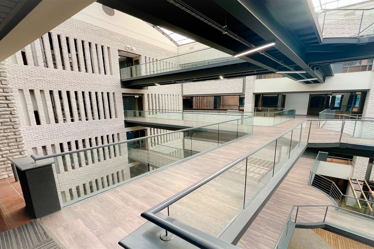 Modern office atrium featuring multi-level suspended walkways, glass balustrades, and architectural brickwork under a large skylight.