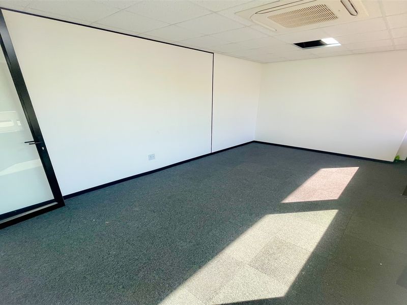 A vacant office space featuring carpet tiles, a suspended ceiling with integrated air conditioning, and a modern glass partition door.