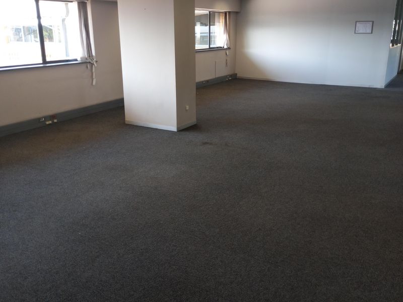 An open-plan office space featuring a suspended ceiling, recessed lighting, and carpeted flooring, offering a versatile layout for professional use.