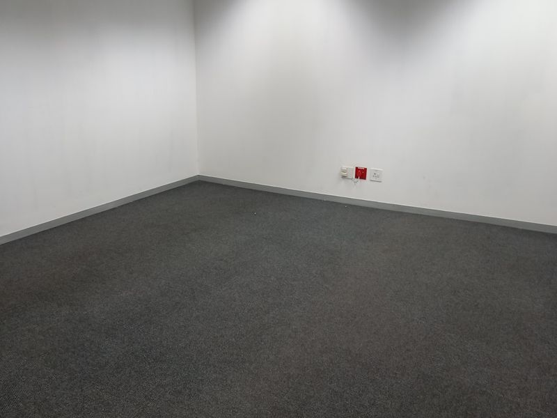 A clean, empty office space featuring neutral walls, grey carpeting, recessed lighting, and integrated ceiling air conditioning.