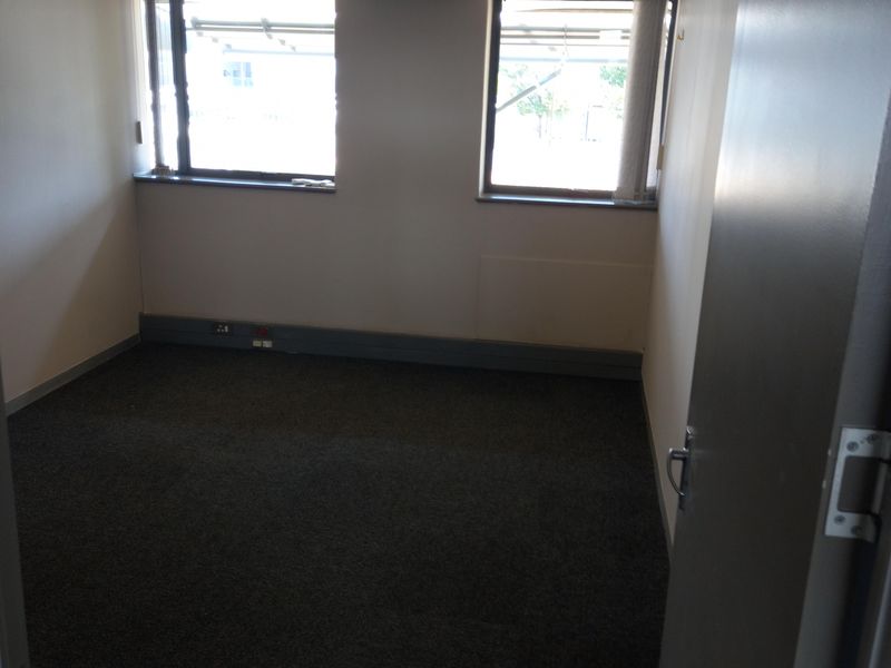 A vacant office space featuring carpeted flooring, recessed ceiling lighting, and a wall-mounted split-system air conditioning unit.