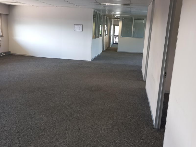 A spacious, empty open-plan office area featuring neutral carpeting, suspended ceilings with recessed lighting, and glass partition walls.