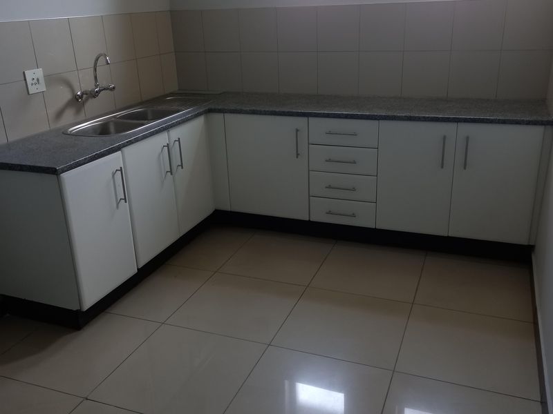 A clean, functional office kitchenette featuring white cabinetry, granite countertops, a stainless steel sink, and neutral tiled flooring.