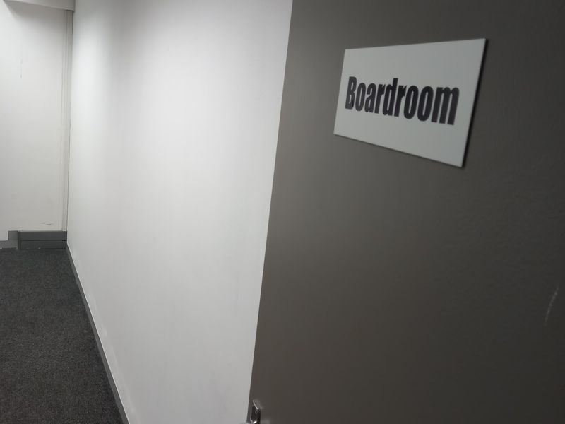 A view of an office hallway featuring grey carpet flooring, white walls, and a door marked with boardroom signage.