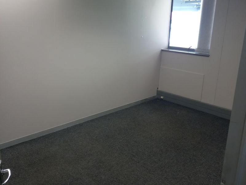 A clean, empty office space featuring grey carpet flooring, a suspended ceiling, and a wall-mounted split-system air conditioning unit.