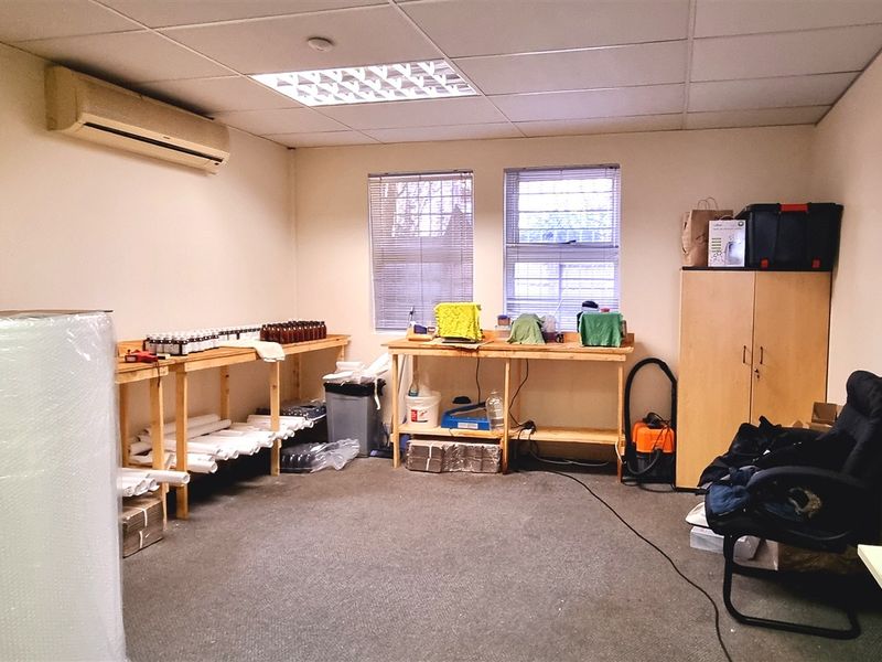 A functional office space featuring a suspended ceiling, wall-mounted air conditioning, and carpeted flooring, suitable for a variety of business or storage uses.