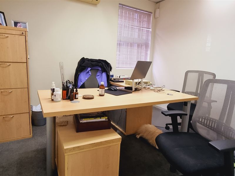 A functional office space featuring carpeted flooring, window blinds, and a wall-mounted air conditioning unit.