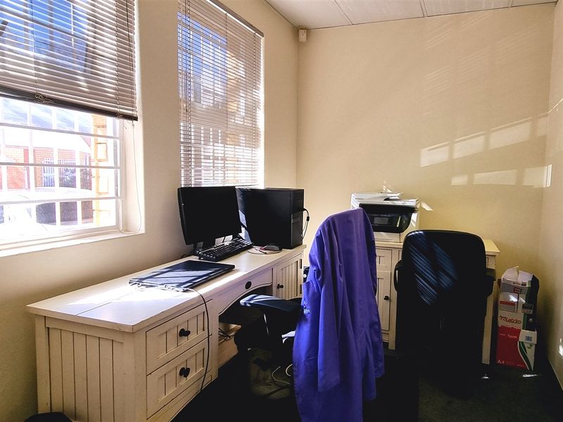 A functional office space featuring large windows with security bars and venetian blinds, providing natural light and a practical work environment.