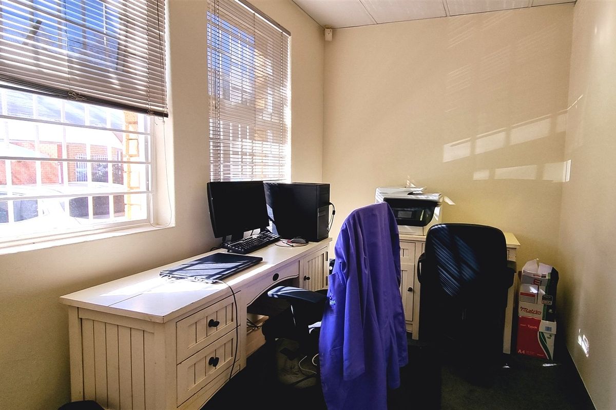 A functional office space featuring large windows with security bars and venetian blinds, providing natural light and a practical work environment.