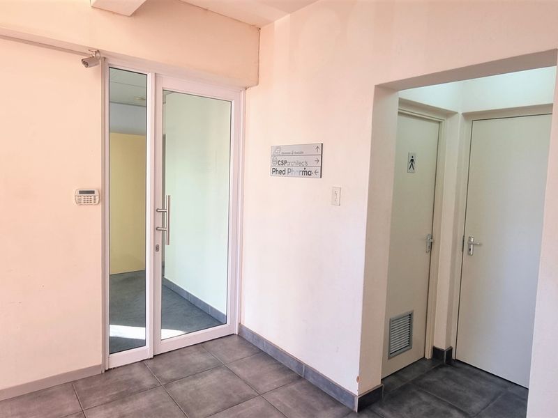 A functional office lobby or hallway area featuring tiled flooring, glass entry door, and directional signage for building occupants.