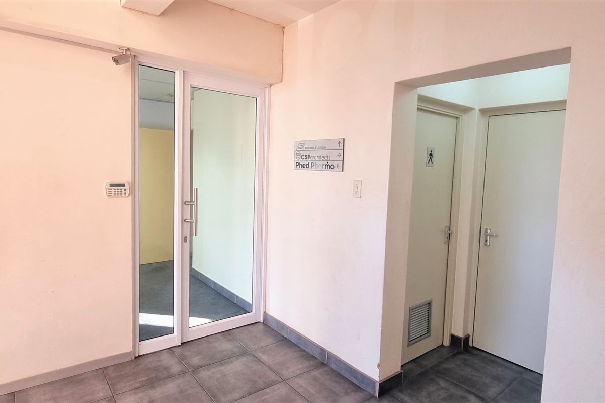 A functional office lobby or hallway area featuring tiled flooring, glass entry door, and directional signage for building occupants.