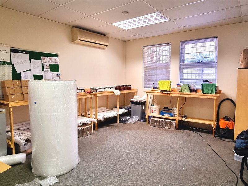 A functional office space featuring a suspended ceiling, wall-mounted air conditioning, and carpeted flooring, currently utilized for storage and workspace operations.