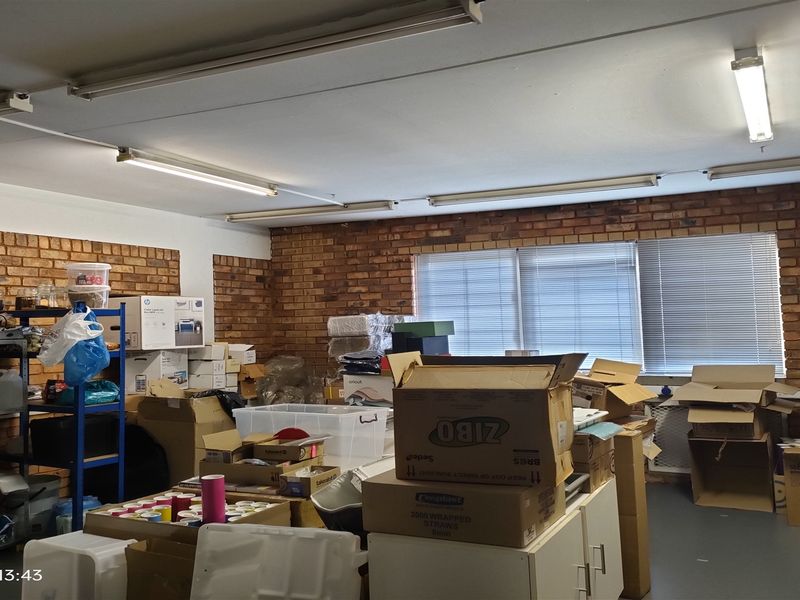 Industrial utility space featuring exposed brick walls, functional fluorescent strip lighting, and venetian blinds, currently utilized for storage.