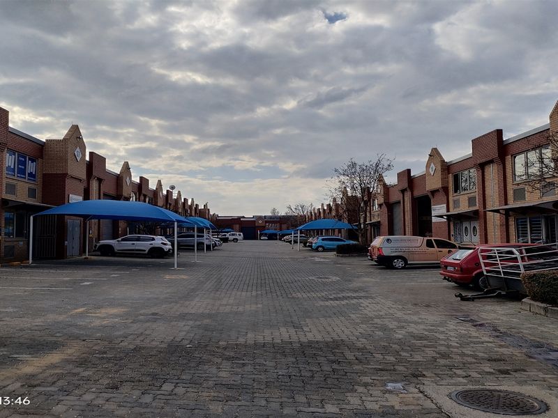 Industrial business park complex featuring a central paved driveway, multiple unit entrances with roller shutter doors, and dedicated shade cloth parking bays.