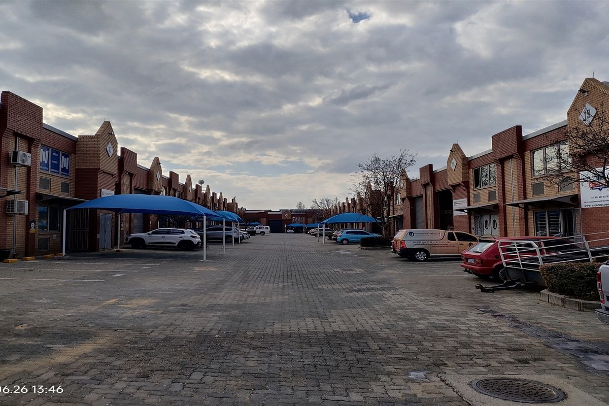 Industrial business park complex featuring a central paved driveway, multiple unit entrances with roller shutter doors, and dedicated shade cloth parking bays.