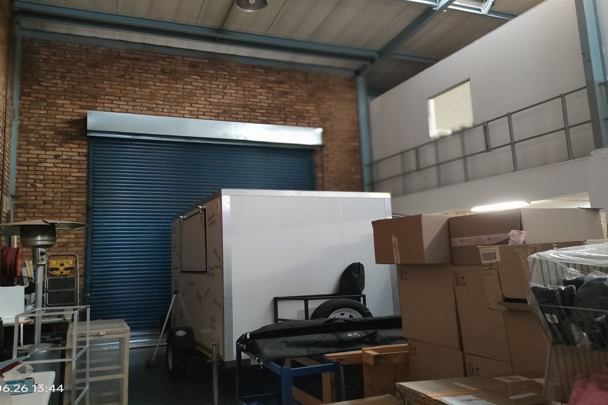 Industrial warehouse space featuring high ceilings with exposed steel beams, a large roller shutter door, and an elevated mezzanine level with metal railings.