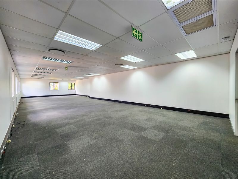 A spacious, open-plan office area featuring a suspended ceiling with recessed lighting, carpeted flooring, and integrated electrical trunking along the walls.