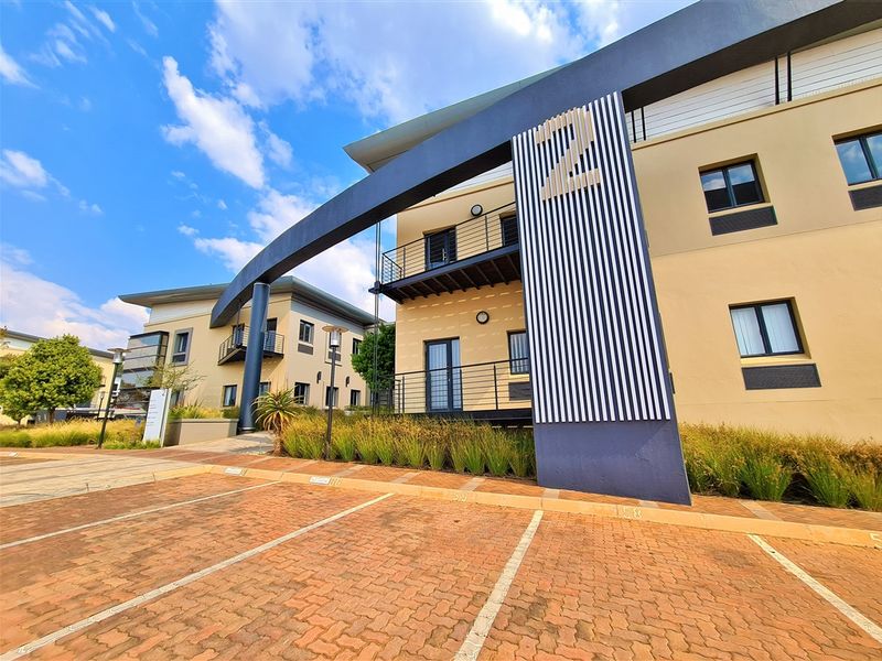 Modern office building exterior featuring a paved parking area, architectural signage, and multi-level balconies with metal railings.