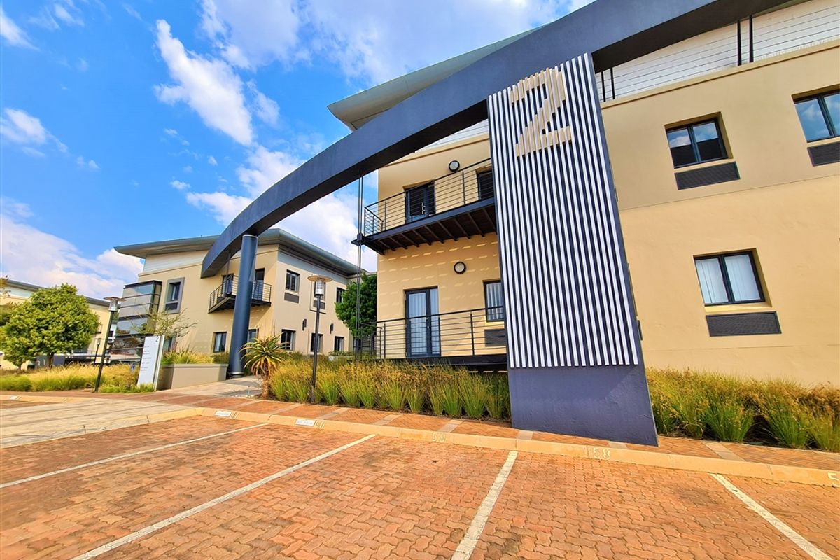 Modern office building exterior featuring a paved parking area, architectural signage, and multi-level balconies with metal railings.