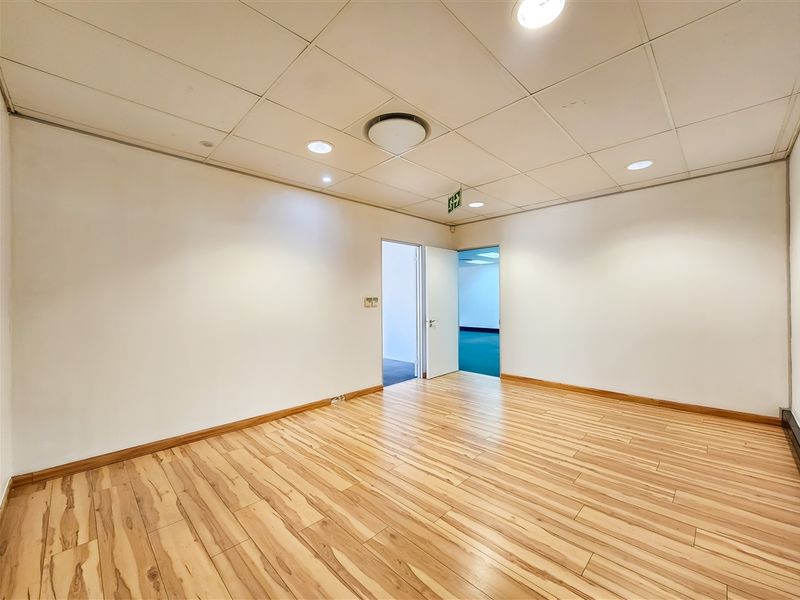 A bright, empty office space featuring laminate wood flooring, a suspended ceiling with recessed lighting, and clean white walls.