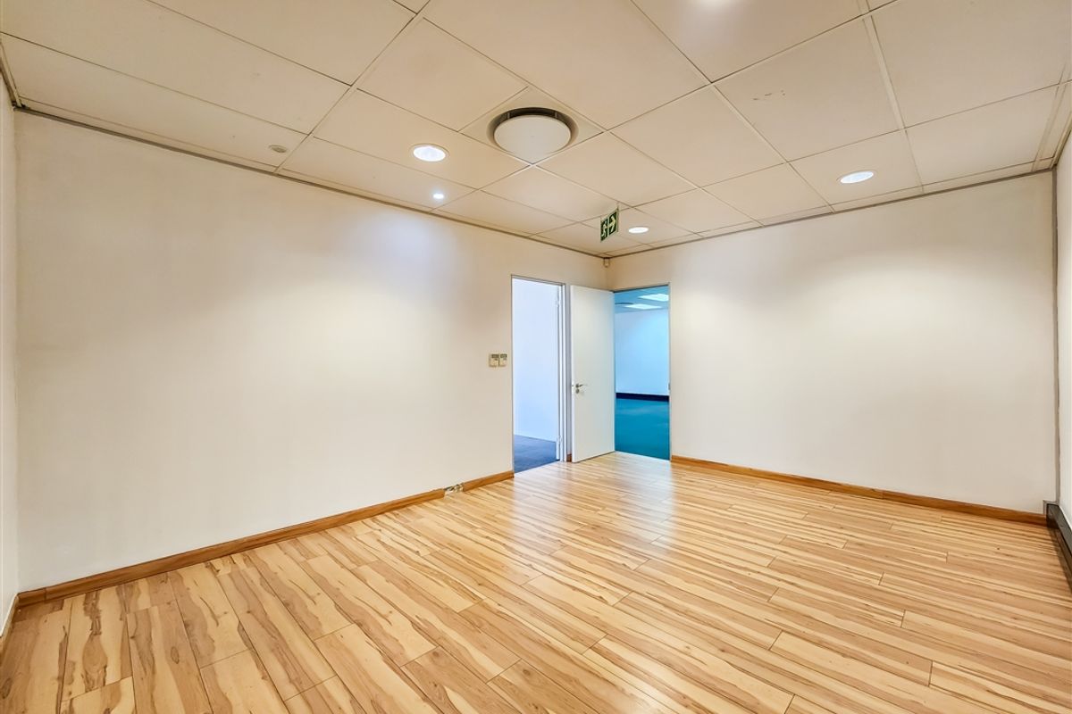 A bright, empty office space featuring laminate wood flooring, a suspended ceiling with recessed lighting, and clean white walls.