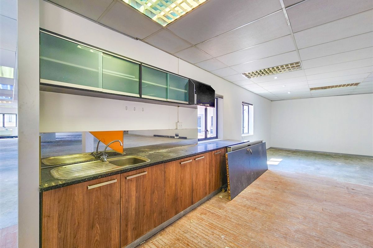 A functional office kitchenette featuring wood-finish cabinetry, a stainless steel sink, and integrated lighting within a drop ceiling.