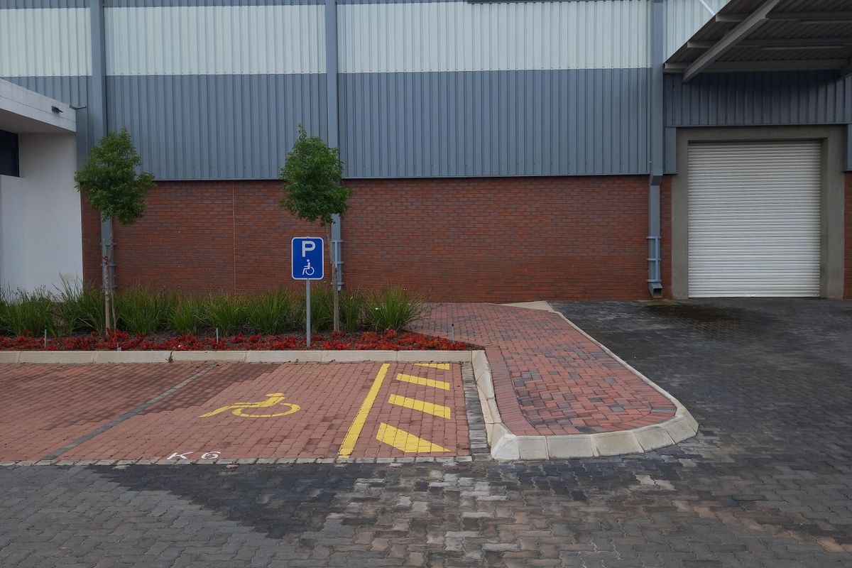 Exterior view of an industrial warehouse facility featuring a roller shutter door, paved parking area, and designated accessible parking bay.
