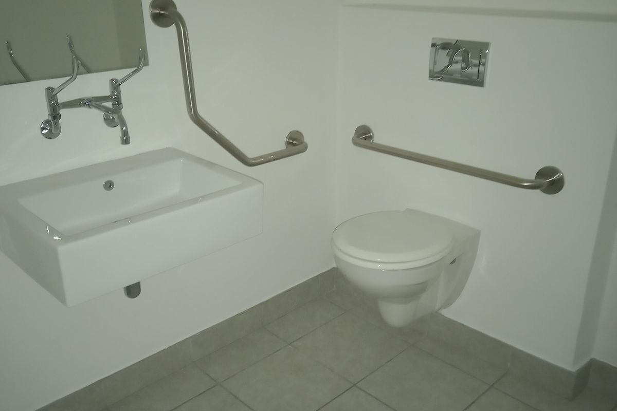 Accessible industrial bathroom featuring a wall-mounted basin, wall-hung toilet, and stainless steel grab rails for enhanced accessibility.