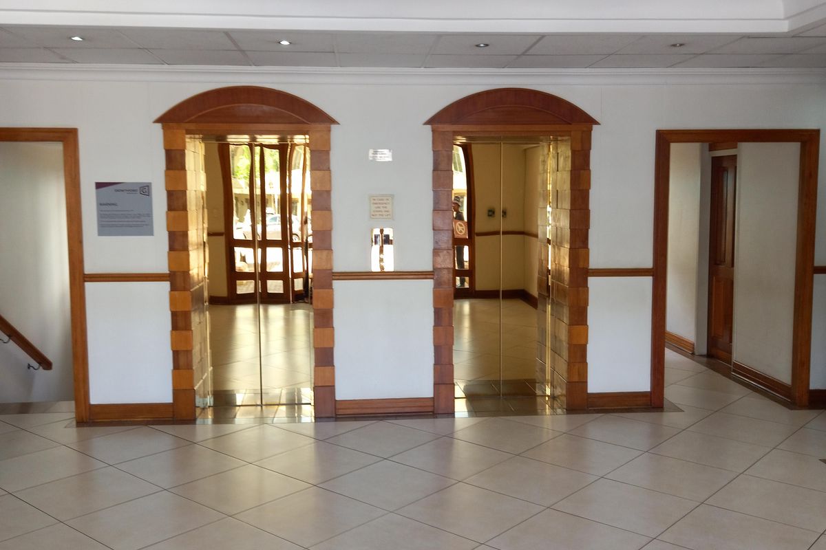A professional office building lobby featuring dual elevator access, decorative wooden door frames, and a distinctive stained glass ceiling fixture.