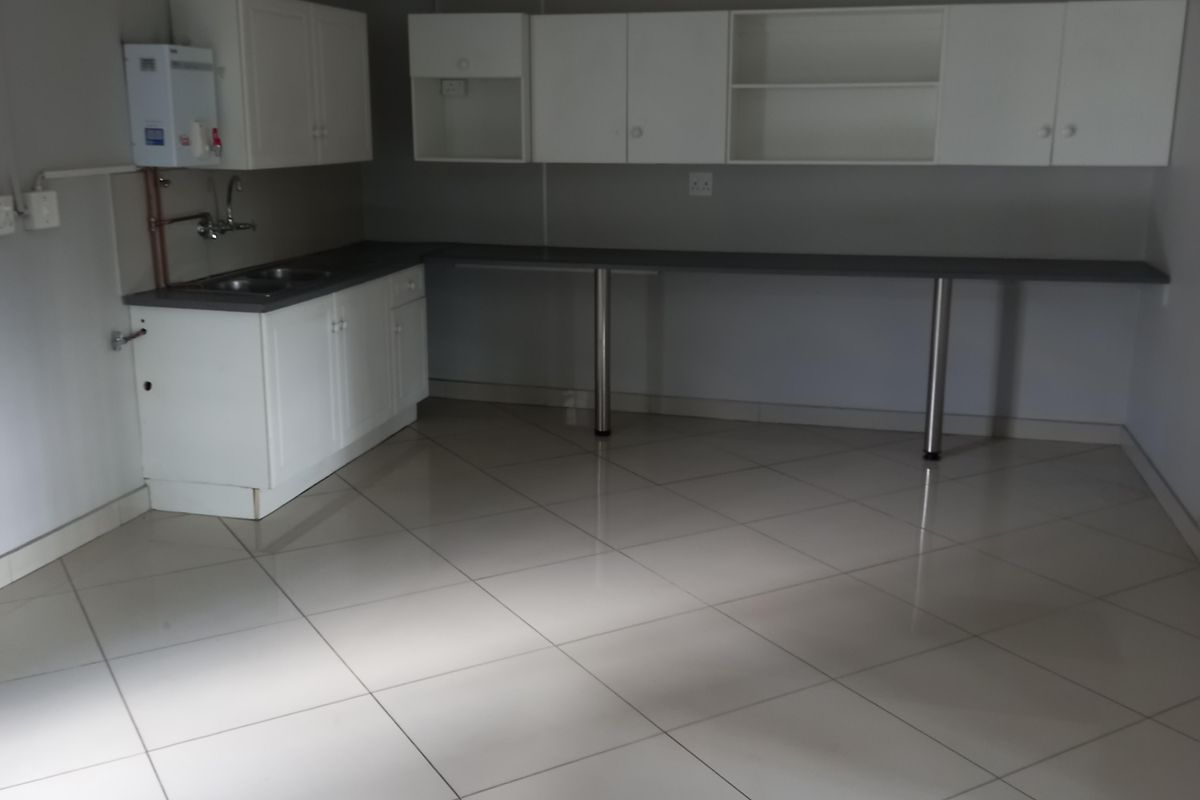 A functional office kitchenette featuring white cabinetry, a stainless steel sink, and a tiled floor, providing a clean and practical workspace.