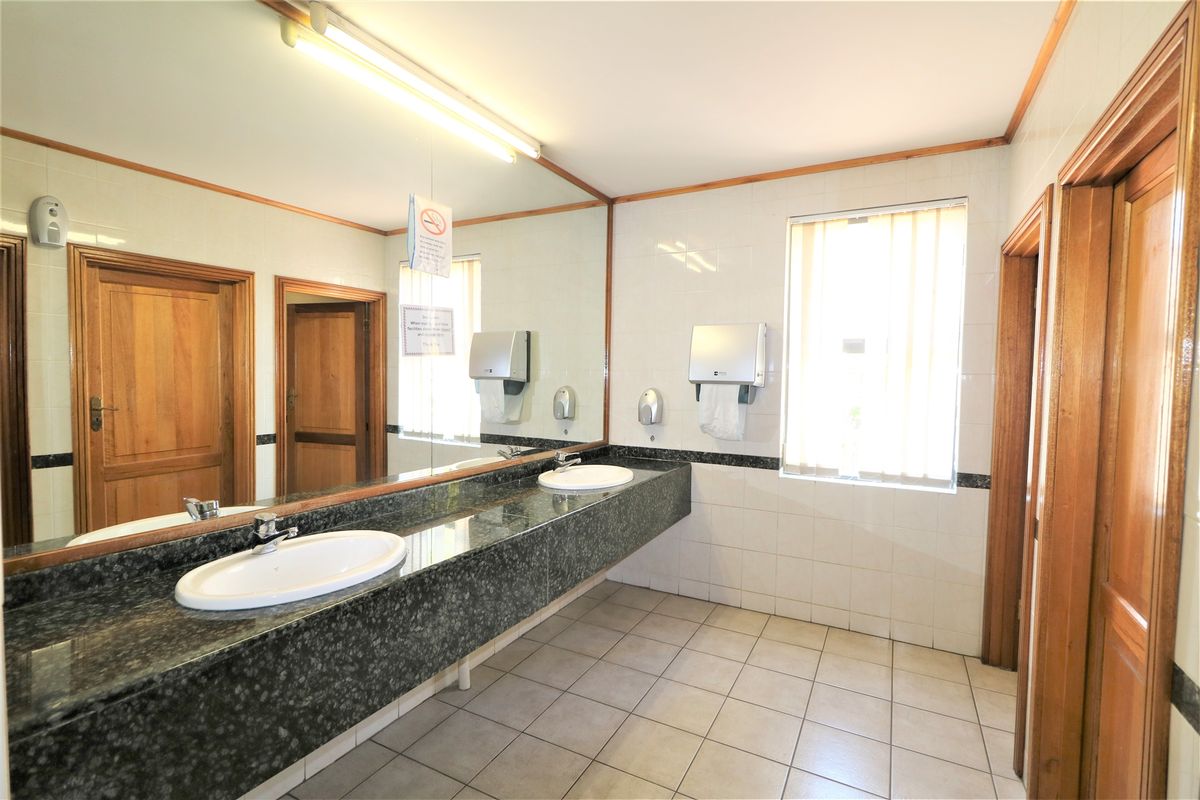 A functional office restroom featuring a long granite vanity with dual drop-in sinks, large wall-mounted mirror, and tiled flooring.