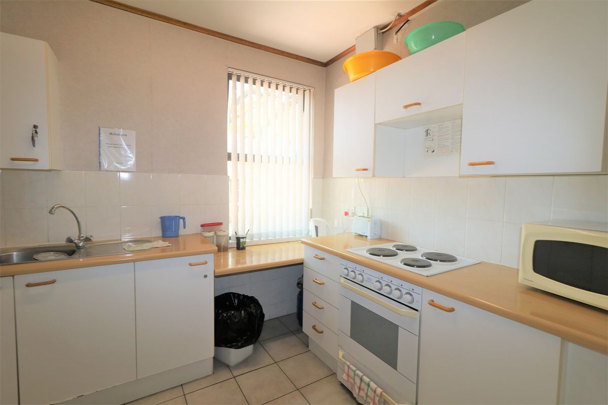 A functional office kitchenette featuring white cabinetry, a built-in electric oven and hob, stainless steel sink, and tiled flooring.