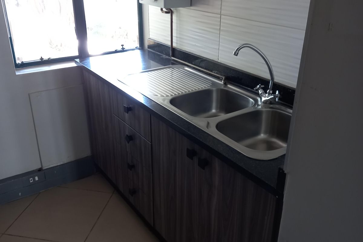 A compact office kitchenette featuring dark wood-grain cabinetry, a stainless steel double sink, and a wall-mounted water heater.