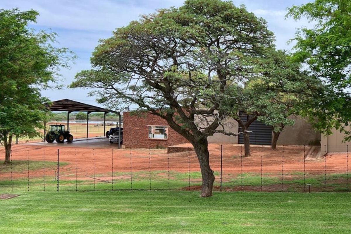 View of the farm property featuring a large open-sided machinery shed, brick building structure, and well-maintained lawn area.