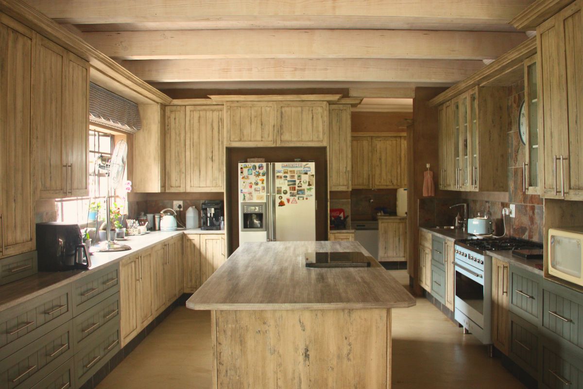 Spacious farmhouse-style kitchen featuring rustic timber cabinetry, exposed ceiling beams, a central island, and integrated cooking appliances.