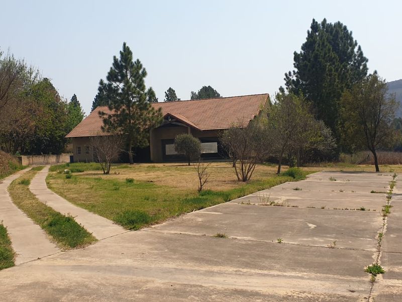 A view of the farm property featuring a large concrete parking area, a driveway, and the main building with a tiled roof.