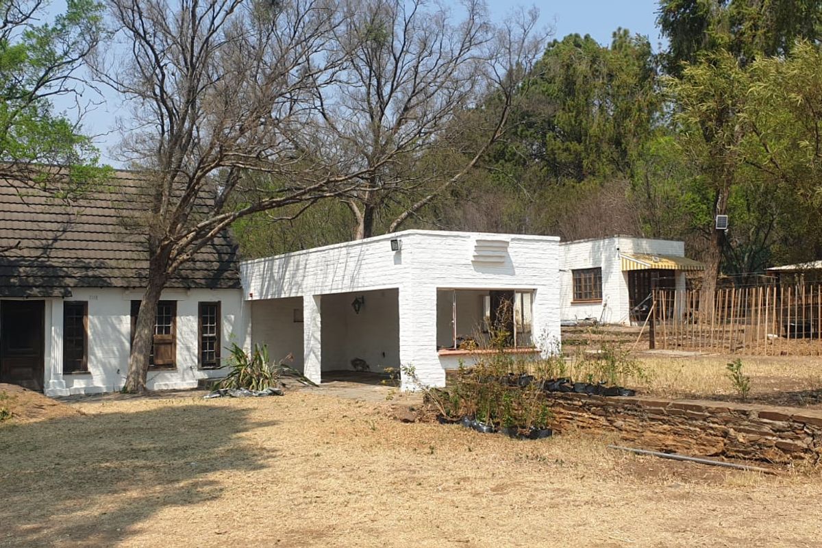 Rear view of the farm property featuring a white brick main house with a covered patio area and a stone retaining wall in the garden.