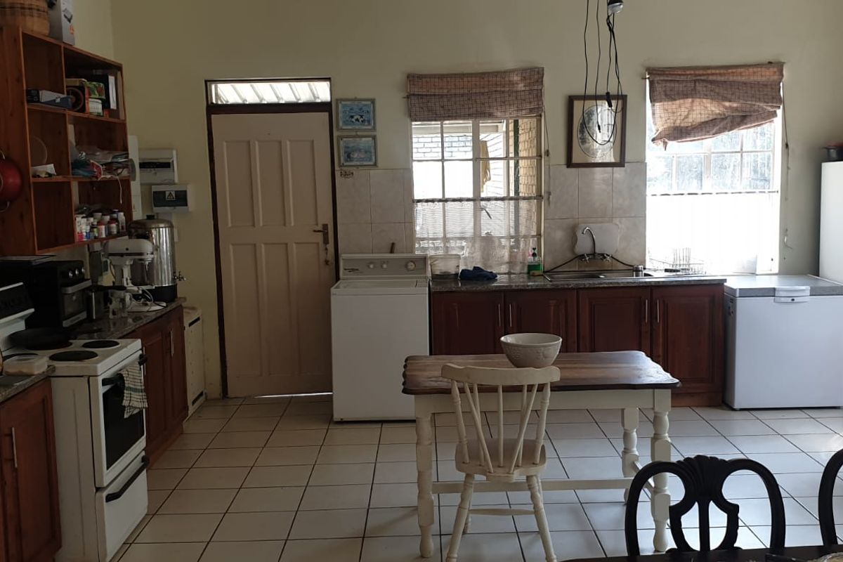 A functional farm-style kitchen featuring wooden cabinetry, stone countertops, tiled flooring, and ample storage space with open shelving.