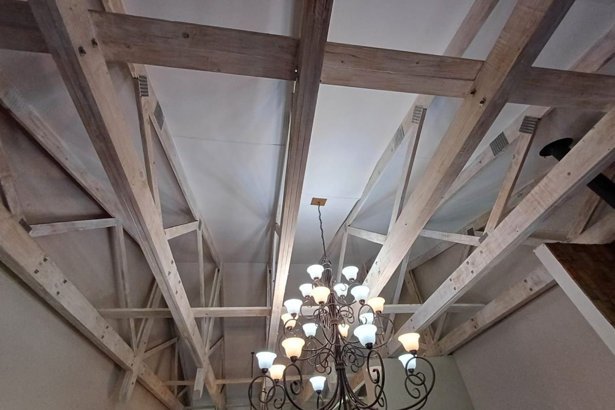 A spacious living area featuring a high vaulted ceiling with exposed timber trusses and a decorative wrought iron chandelier.