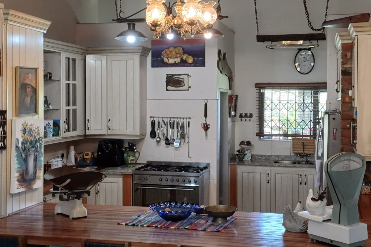 A rustic farmhouse kitchen featuring white cabinetry, stone countertops, a gas stove, and a central wooden breakfast bar with pendant lighting.