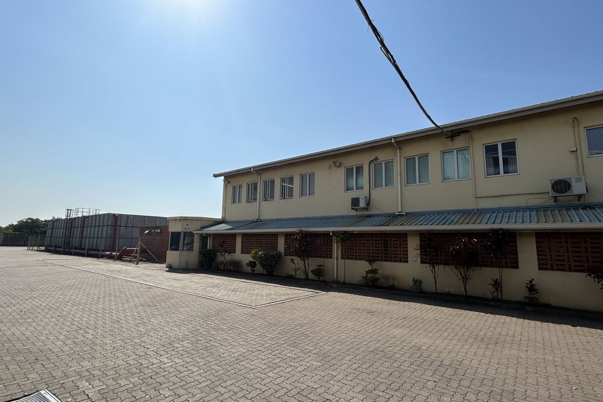 Exterior view of an industrial facility featuring a large paved yard, water storage infrastructure, and a multi-windowed office or administrative building section.