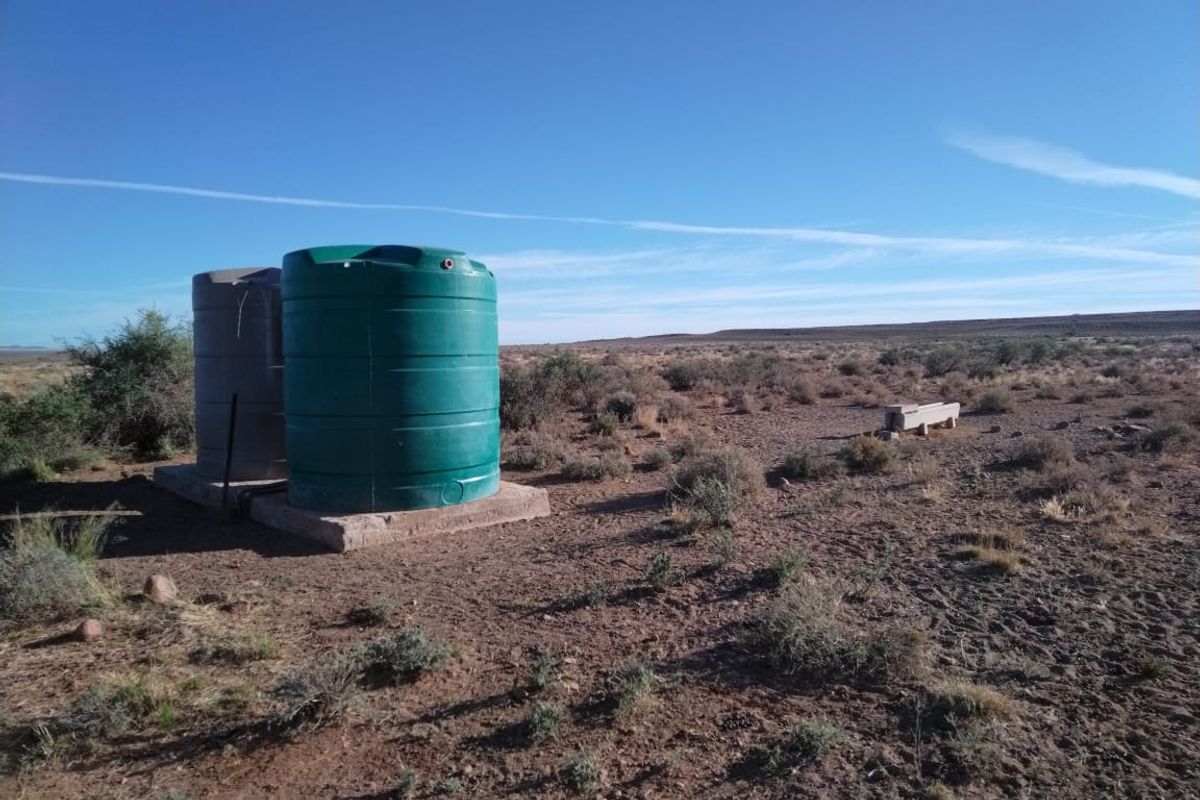Outdoor utility area featuring two large water storage tanks on a concrete base and a nearby livestock water trough in a rural setting.