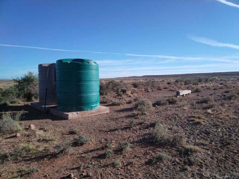 Outdoor utility area featuring two large water storage tanks on a concrete base and a nearby livestock water trough in a rural setting.