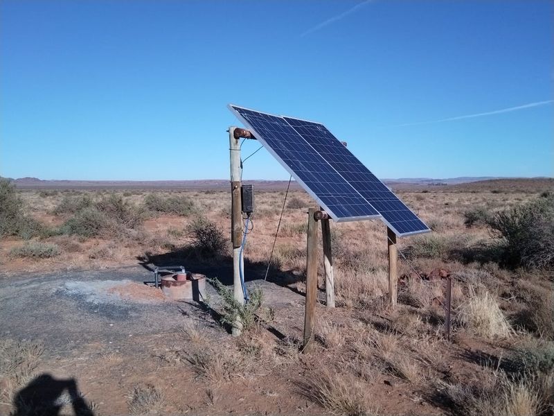 A solar-powered borehole pump installation located in an open field, providing essential water infrastructure for the farm.