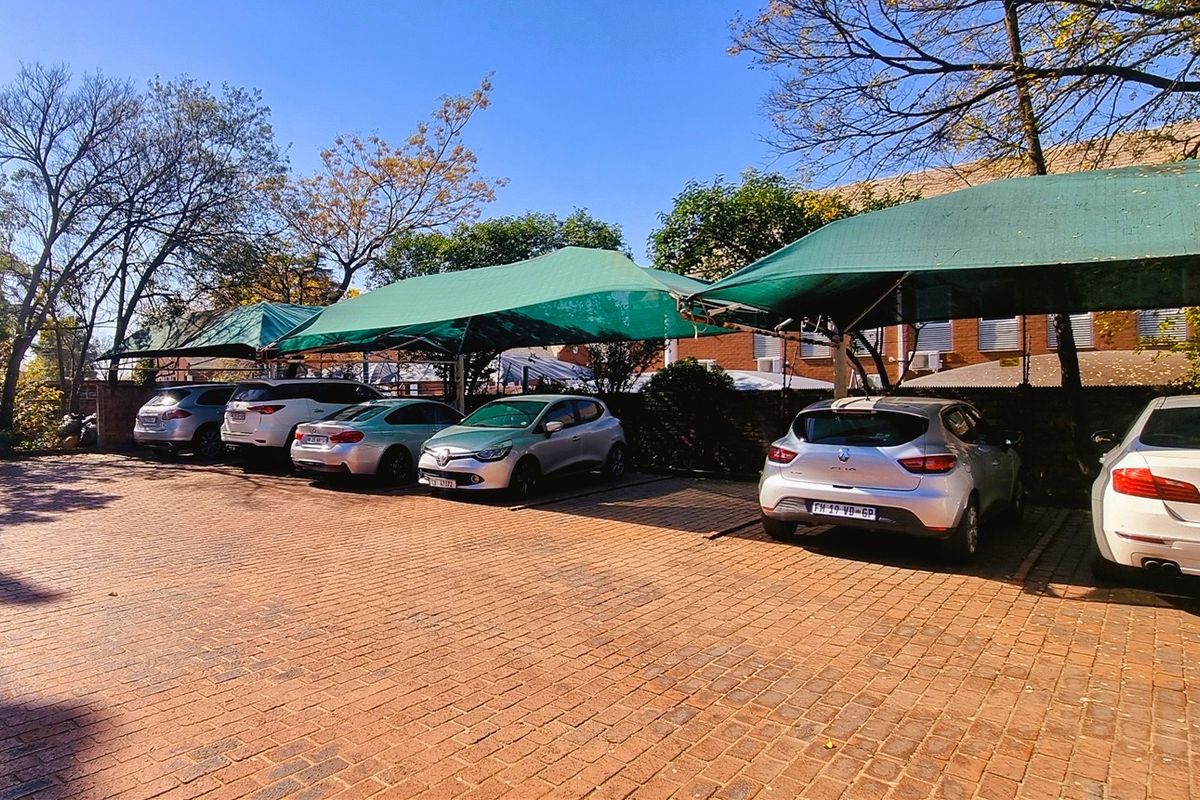 Outdoor parking area featuring paved brick surfacing and multiple green shade cloth carports for vehicle protection.