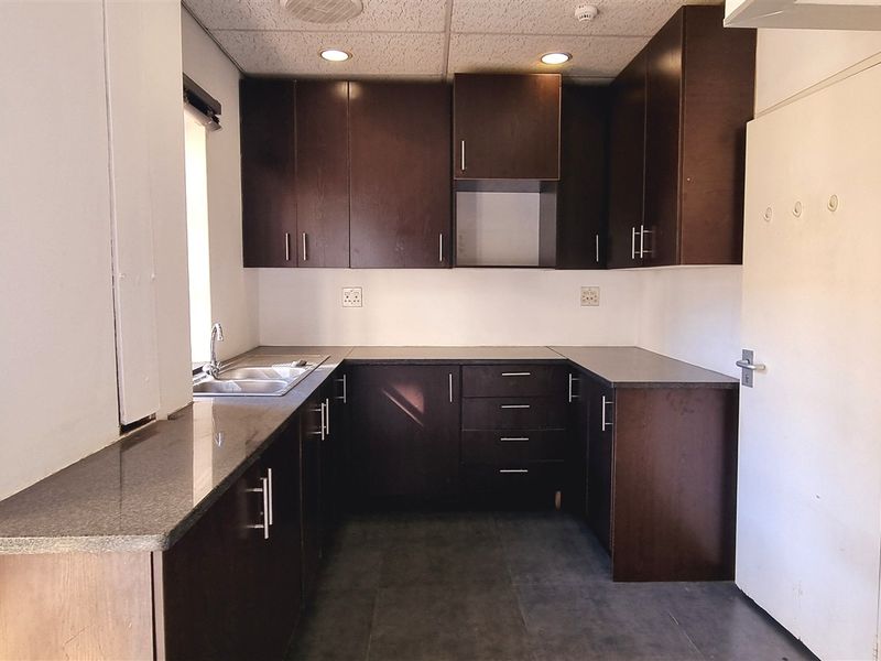A clean, functional office kitchenette featuring dark wood cabinetry, laminate countertops, a stainless steel sink, and recessed lighting in a drop ceiling.