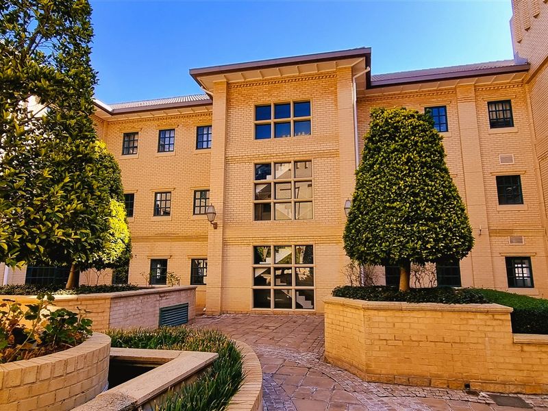 A well-maintained rear courtyard featuring a classic brick facade, paved walkways, and established landscaping within raised brick planters.